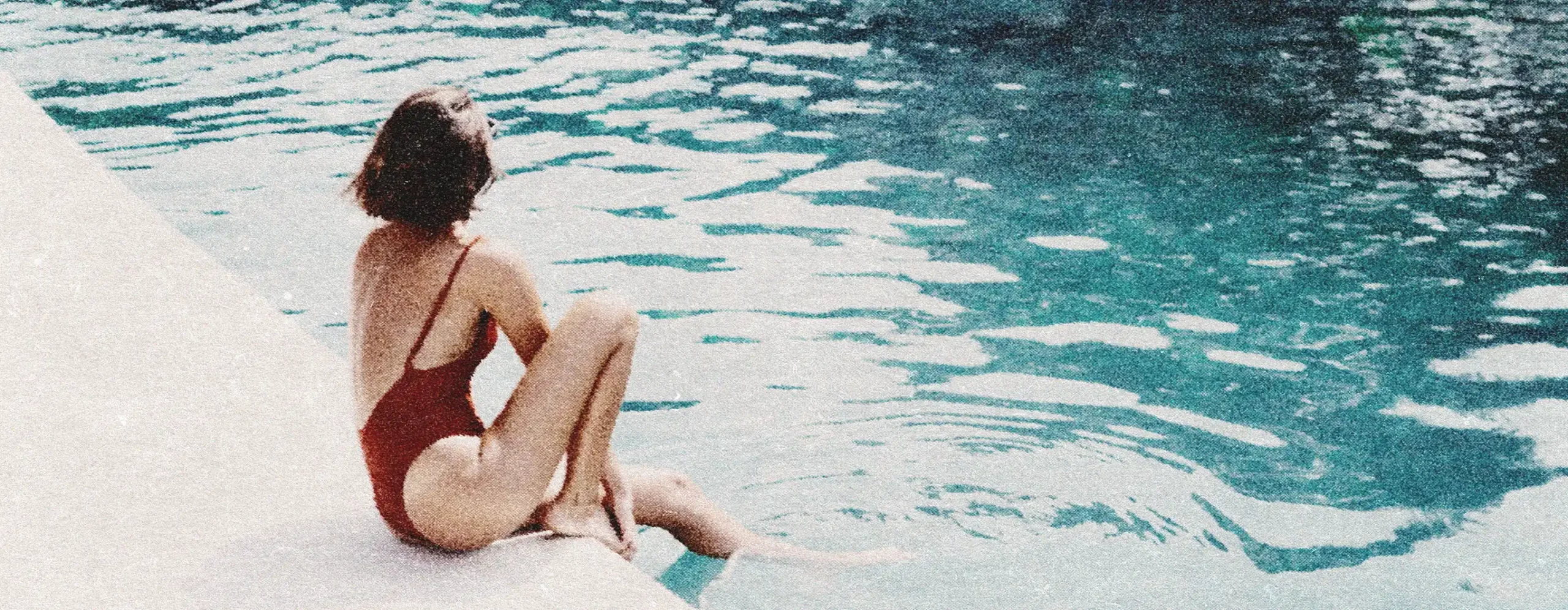 Stylized photo of woman in a red bathing suit sitting at the edge of a pool with her feet in the water.